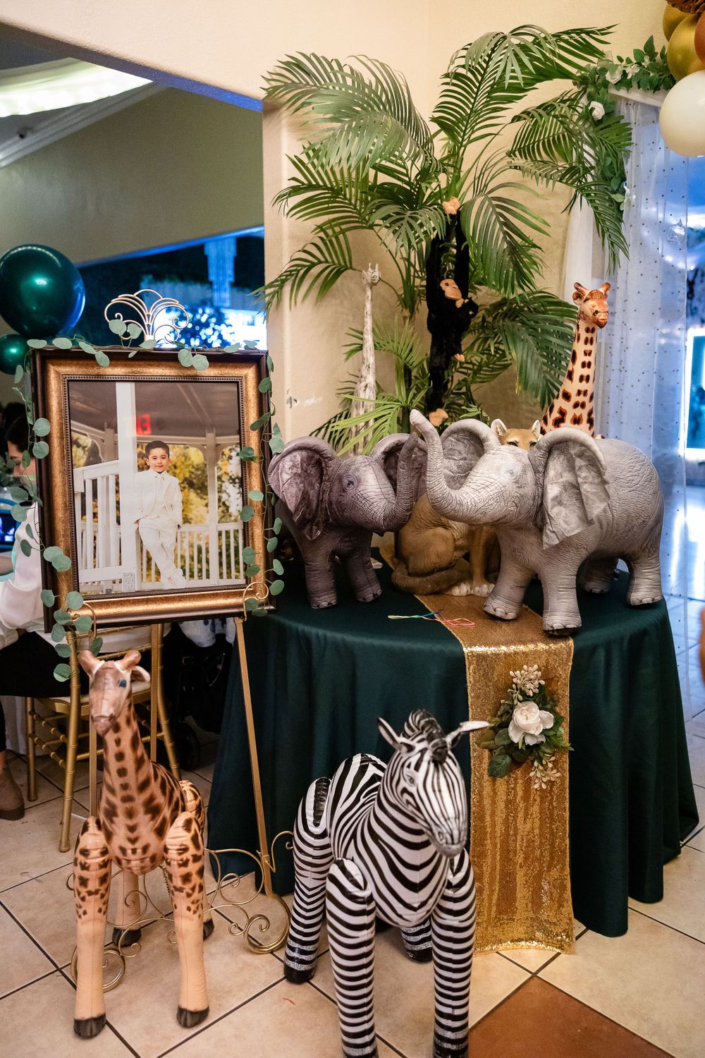 Safari-themed party decor with plush elephants, giraffes, and zebras arranged on dark tablecloths.