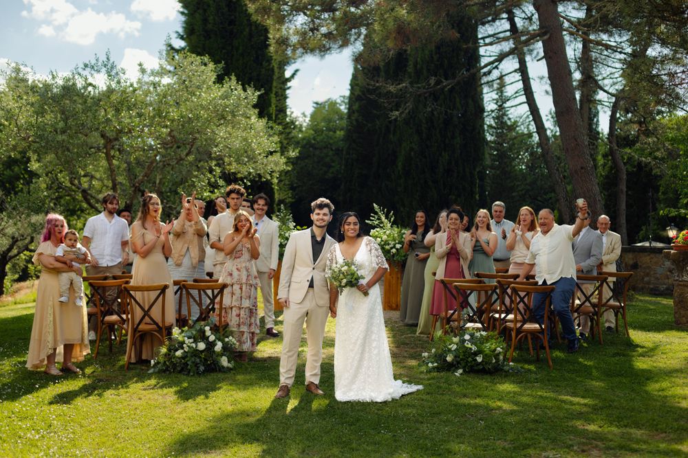 Outdoor wedding celebration with guests gathered in a sunny garden setting.
