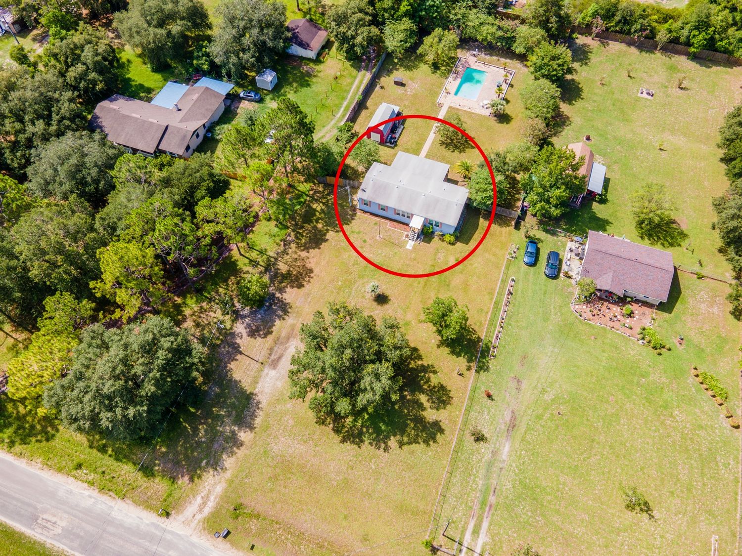 Aerial view of rural property with swimming pool and multiple buildings surrounded by trees.
