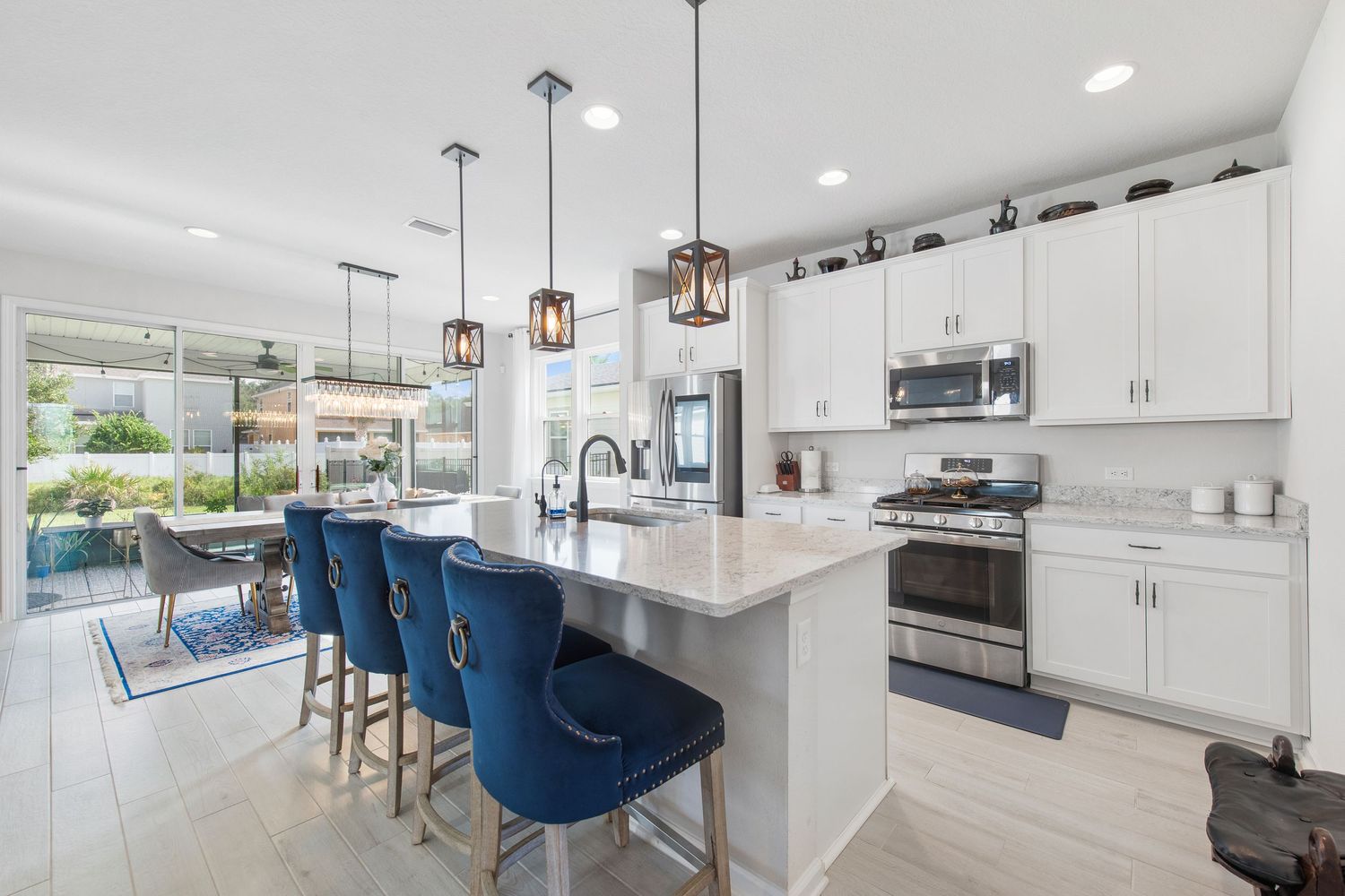 Modern white kitchen with blue bar stools, pendant lights, and marble island countertop in Jacksonville, Florida.
