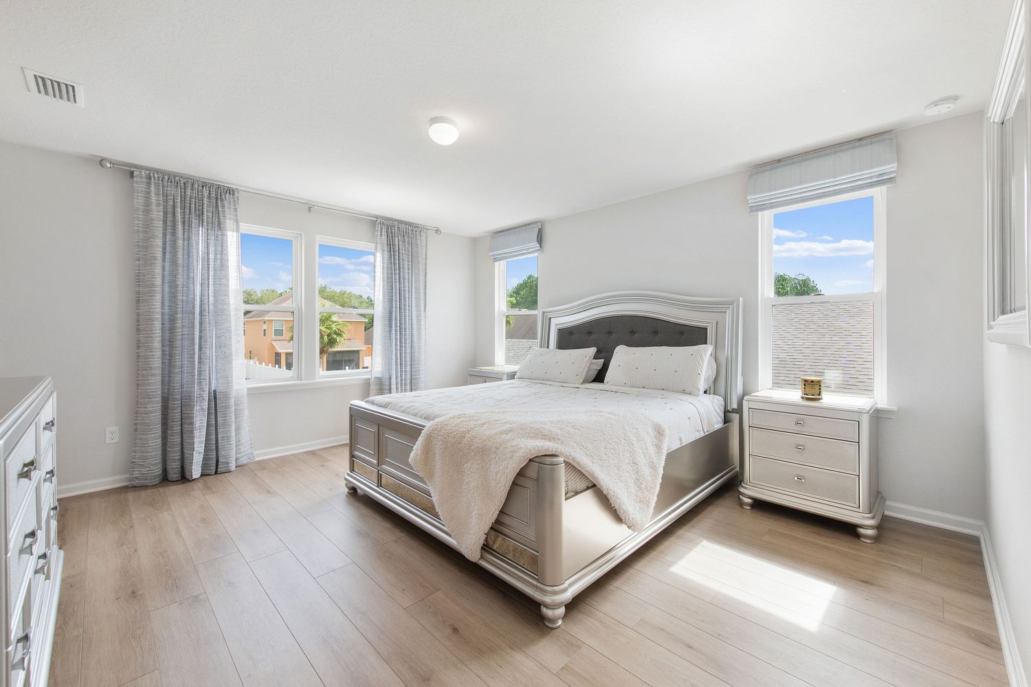 Bright master bedroom with upholstered bed, white furniture, and large windows in Jacksonville, Florida.