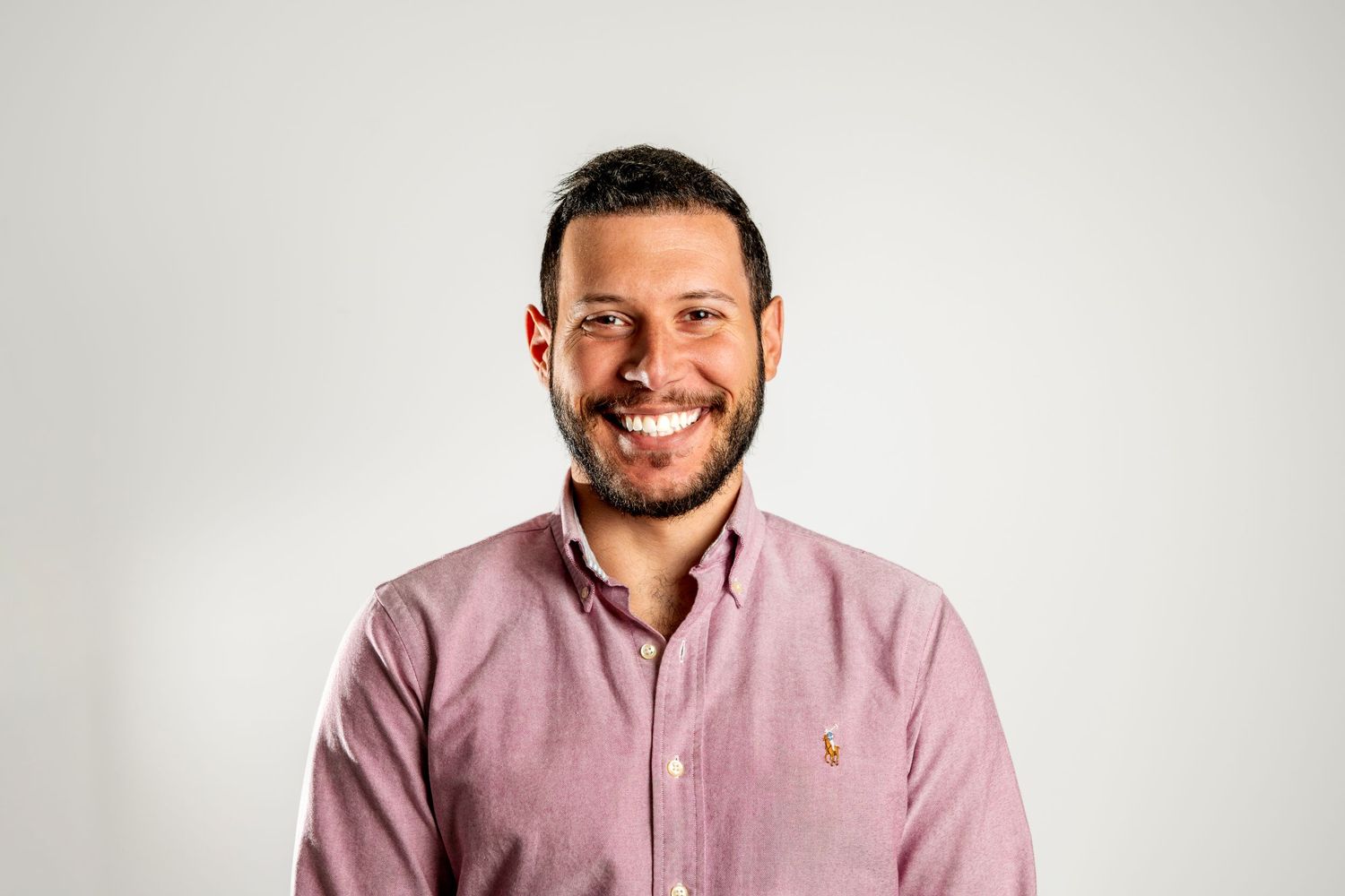 Professional headshot of person wearing a pink button-down shirt against white background.