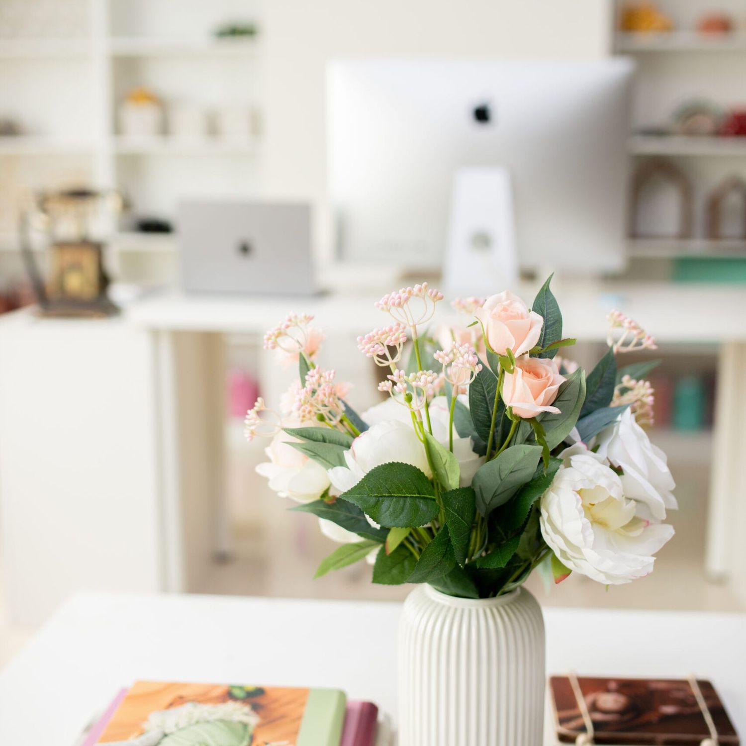 White and pink roses in a ribbed white vase on desk with computer monitor in background.