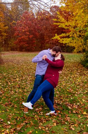 A romantic couple embraces in a fall setting with vibrant red and yellow foliage in the background.