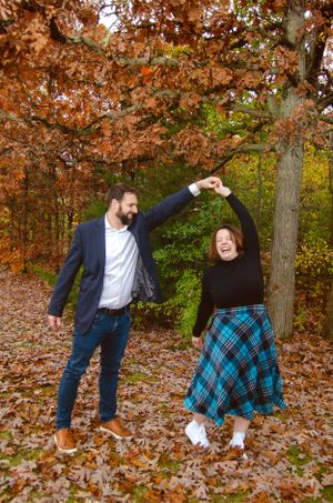 Couple dancing playfully in autumn leaves wearing casual attire.
