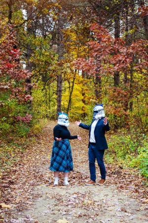 Two figures in warm clothing walking along an autumn forest path with colorful fall foliage.