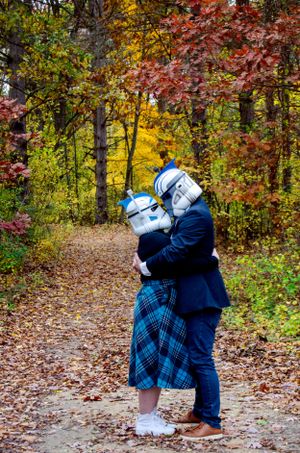A couple wearing stormtrooper masks embraces on a fall foliage covered path.