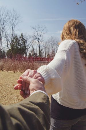 Holding hands while sitting outdoors on a sunny winter day with red bridge in background.