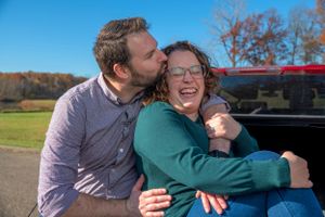 A tender moment shared between a couple in front of a red vehicle on a sunny day.