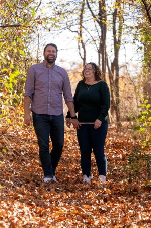 A couple shares a laugh while standing on an autumn trail covered in fallen leaves.
