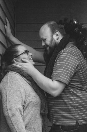 Black and white intimate portrait showing affection against a wooden wall.