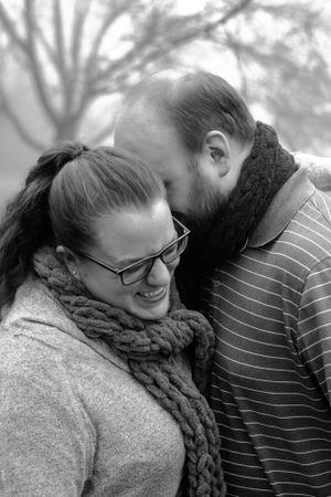A tender moment captured in black and white between a couple wearing scarves on a foggy day.