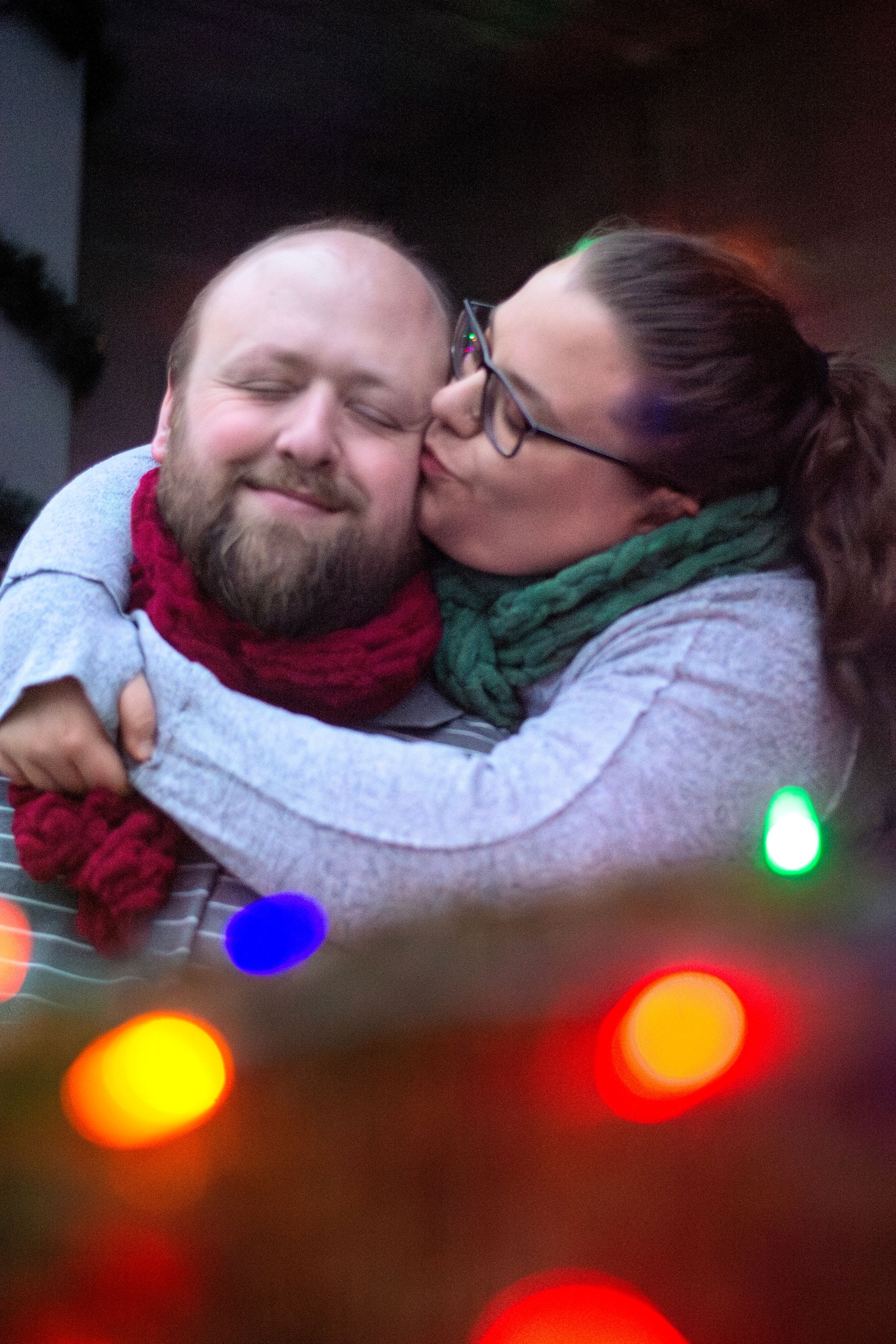 Intimate holiday portrait with festive lights and warm winter accessories.