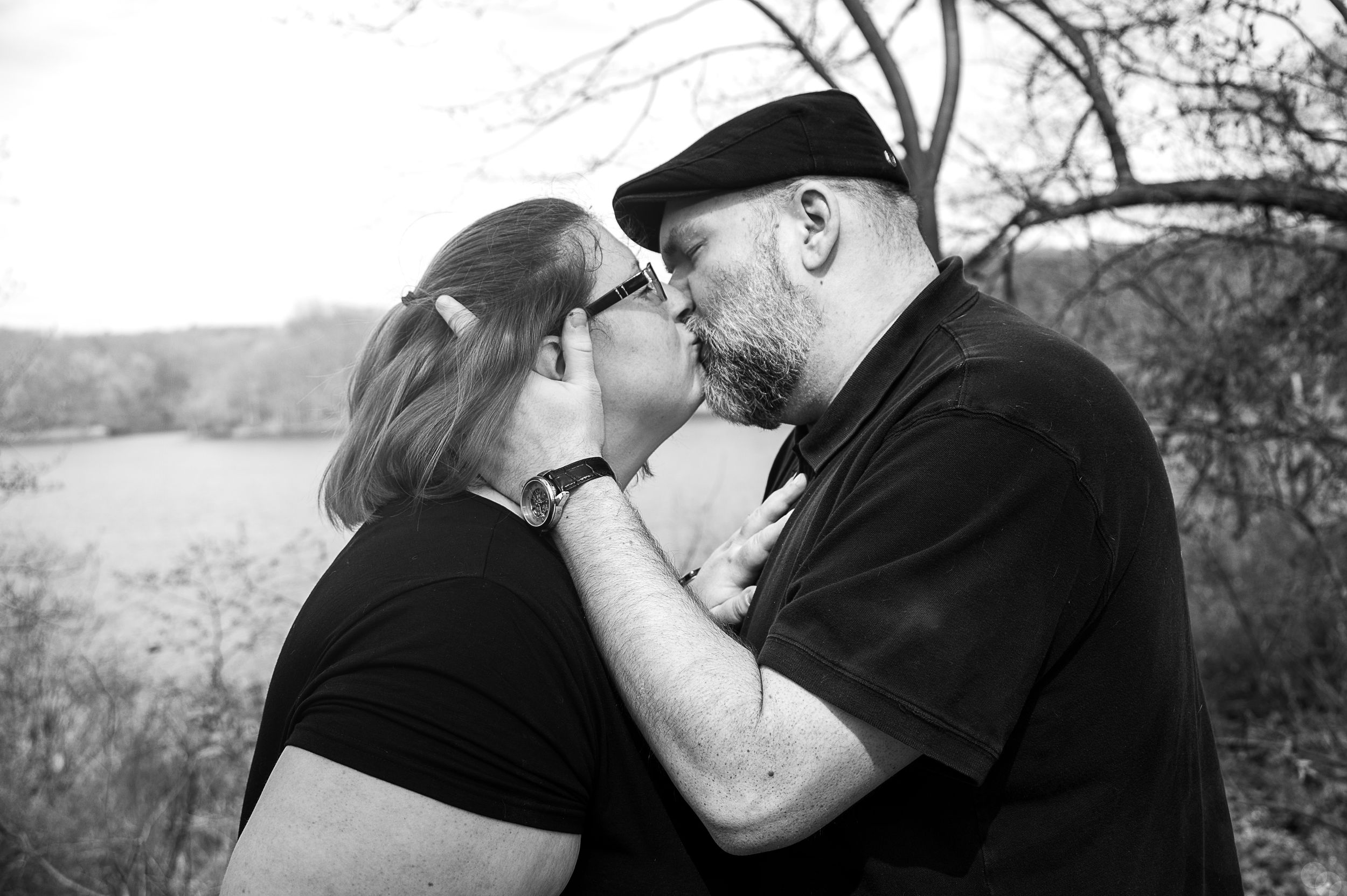 A romantic black and white outdoor photo of a couple in casual attire sharing an intimate moment in a natural setting.