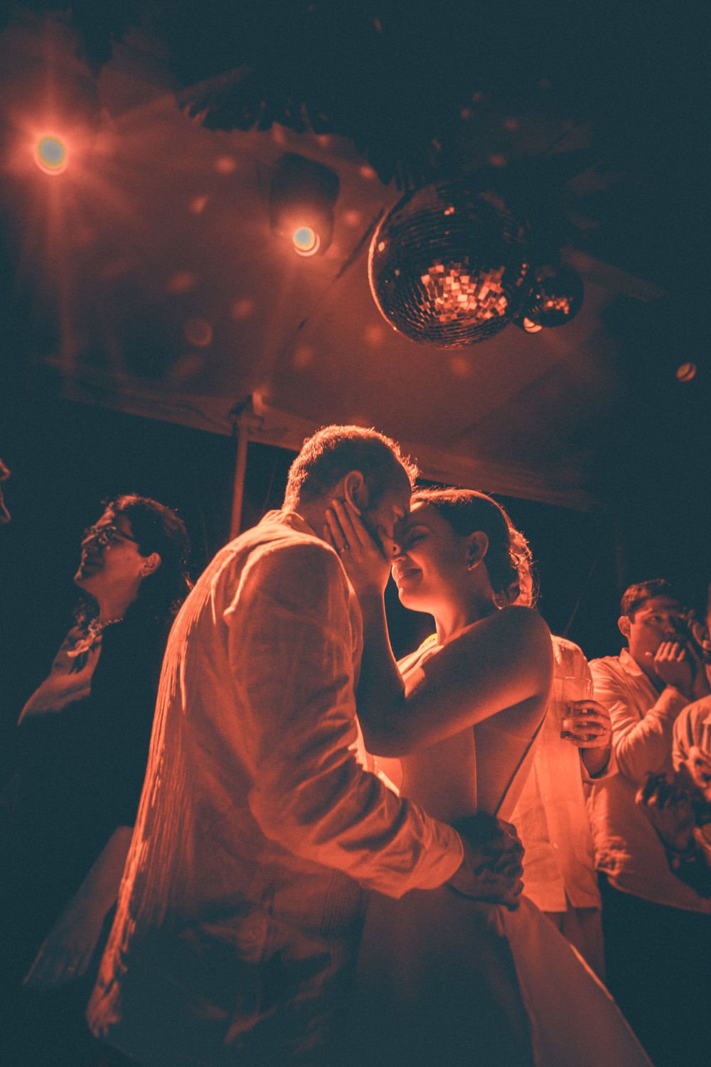 Couple shares intimate dance moment under red lighting at reception.