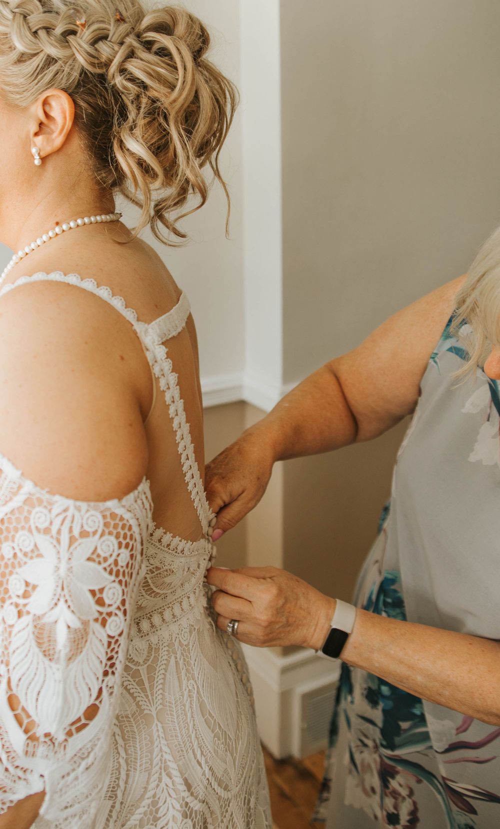 Close-up details of a bride getting ready in an intricate lace wedding dress with pearl buttons and straps.