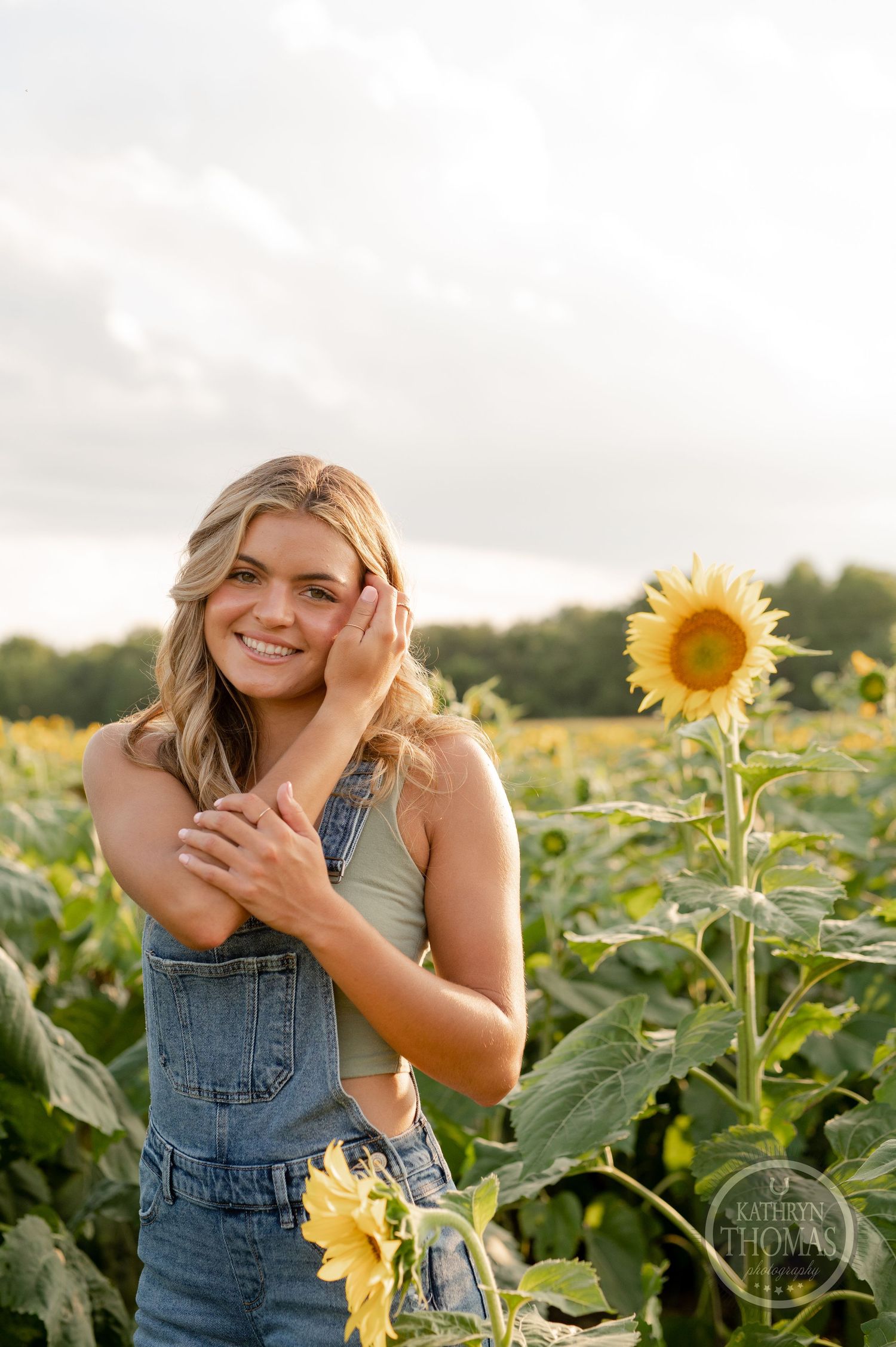 A candid summer portrait showing someone in overalls laughing among tall sunflowers.
