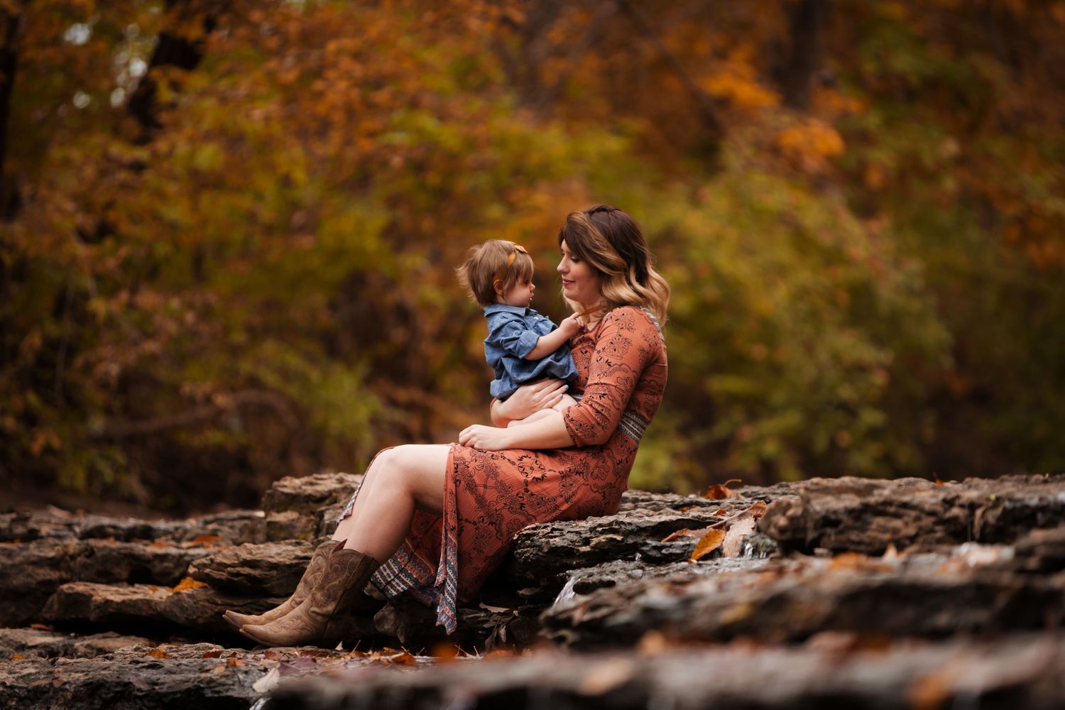 Woman and child sitting on rocky outcrop surrounded by autumn foliage.
