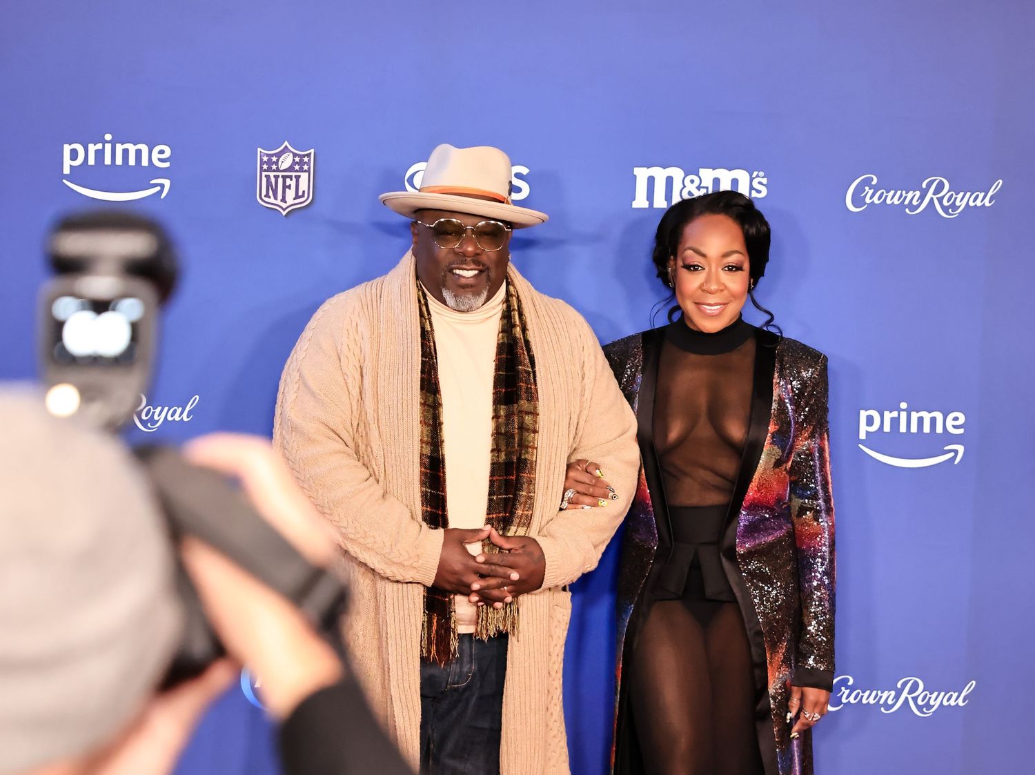 Two attendees pose together at Super Bowl event against blue sponsor backdrop.