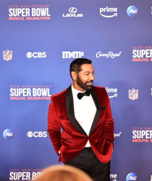 Stylish guest in red velvet tuxedo jacket poses at Super Bowl media event.