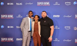 Three attendees pose together on blue backdrop at Super Bowl event.