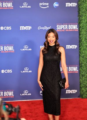 Woman in black fitted evening gown poses on red carpet at Super Bowl celebration event.
