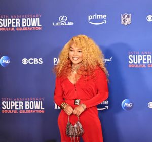 Attendee in bright red dress poses at Super Bowl Soulful Celebration against blue backdrop.