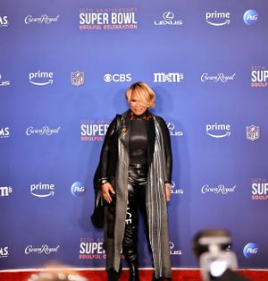 Guest wearing all-black leather ensemble poses on red carpet at Super Bowl celebration.