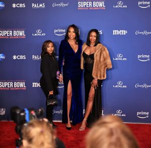 Three people in formal attire pose together at Super Bowl celebration event.