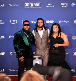 Three guests pose together on red carpet at Super Bowl celebration with backdrop.