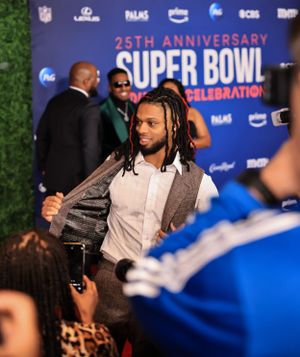 A guest arrives at the Super Bowl Soulful Celebration against a backdrop with NFL and sponsor logos.