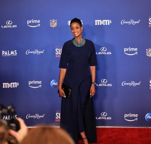 Attendee in navy dress poses at Super Bowl Soulful Celebration against blue backdrop.