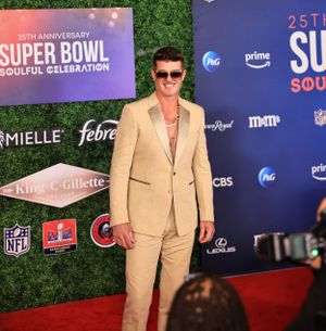 Person in tan suit poses confidently on red carpet at Super Bowl Soulful Celebration event.