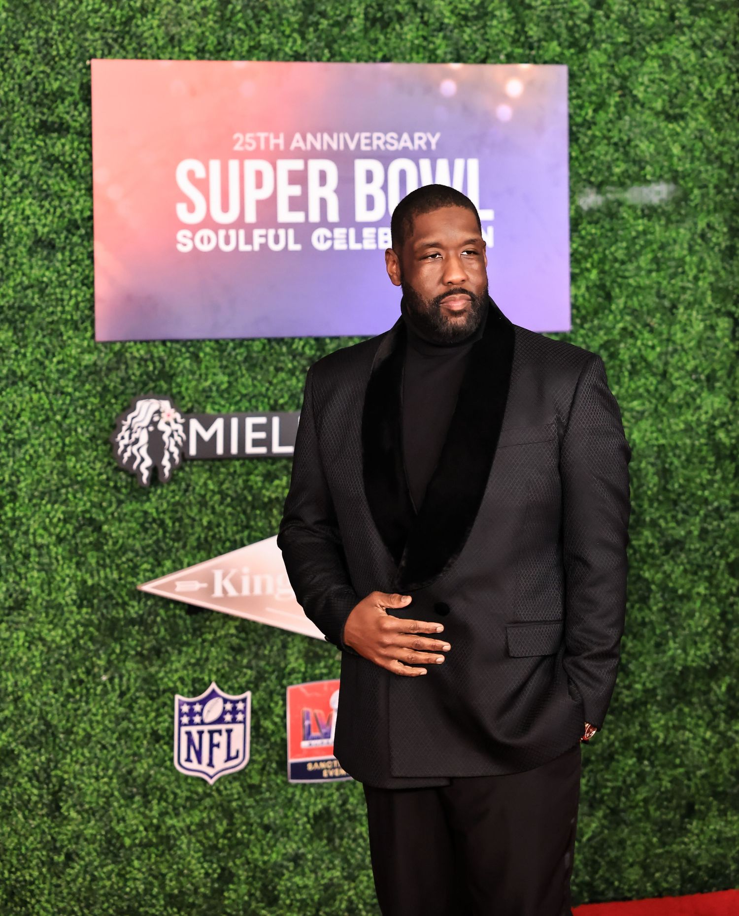 A well-dressed attendee poses against a hedge wall backdrop at the Super Bowl celebration event.