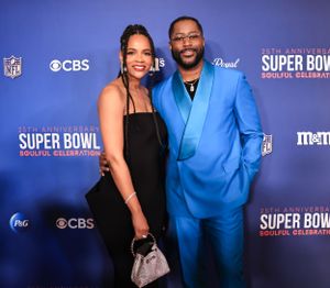 Couple poses on blue carpet at Super Bowl Soulful Celebration, with man wearing bright blue suit.