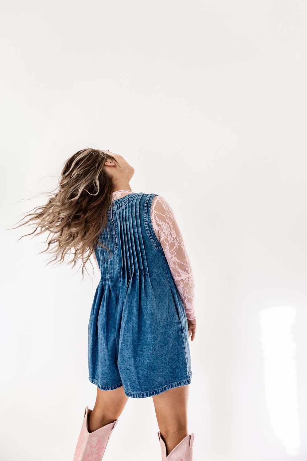 Wyoming Photographer
Person in denim dress and cowboy boots dances with hair flowing in white room against minimalist backdrop.