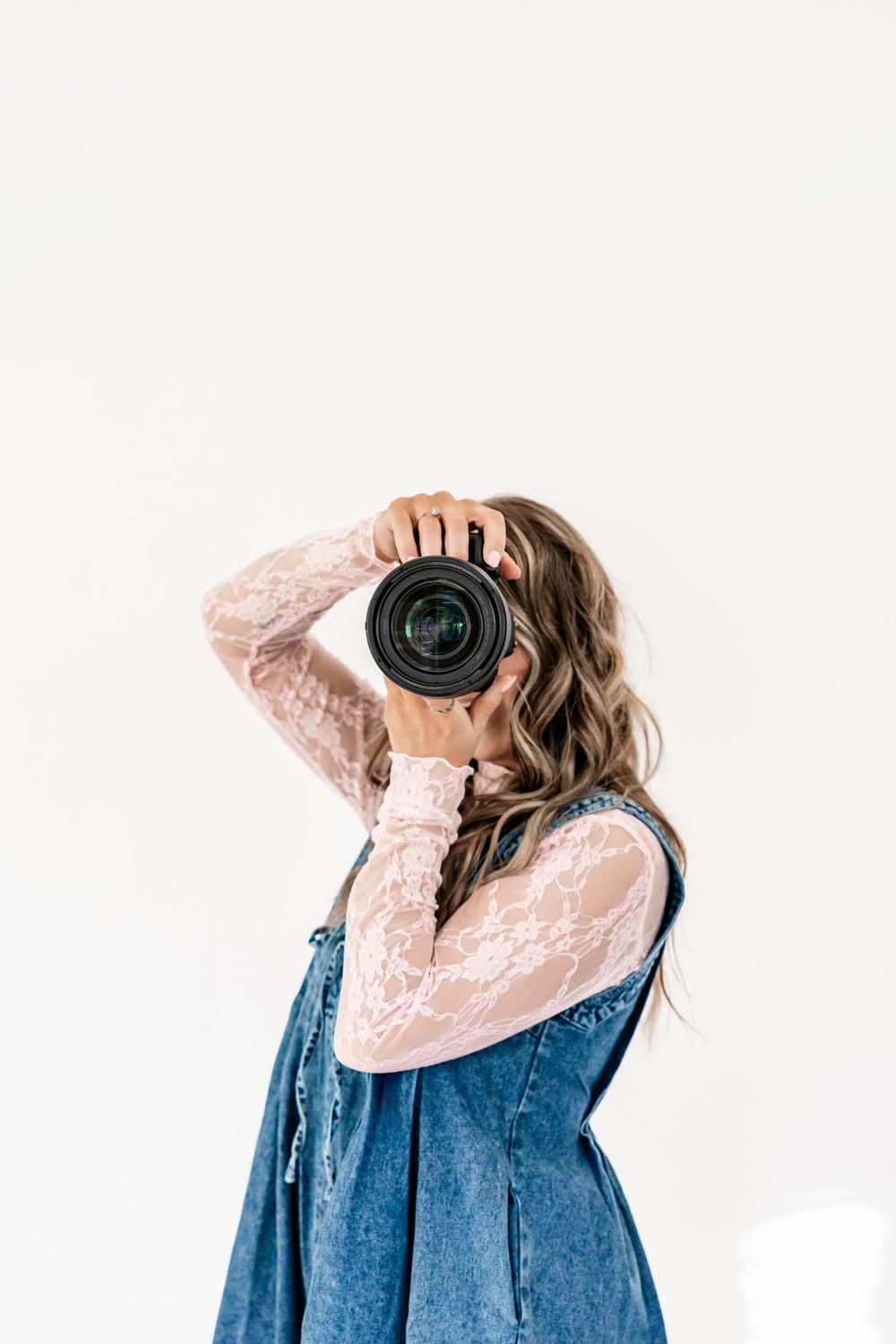 Wyoming Photographer
Photographer wearing denim dress and lace blouse holds camera to take photo against white background.
