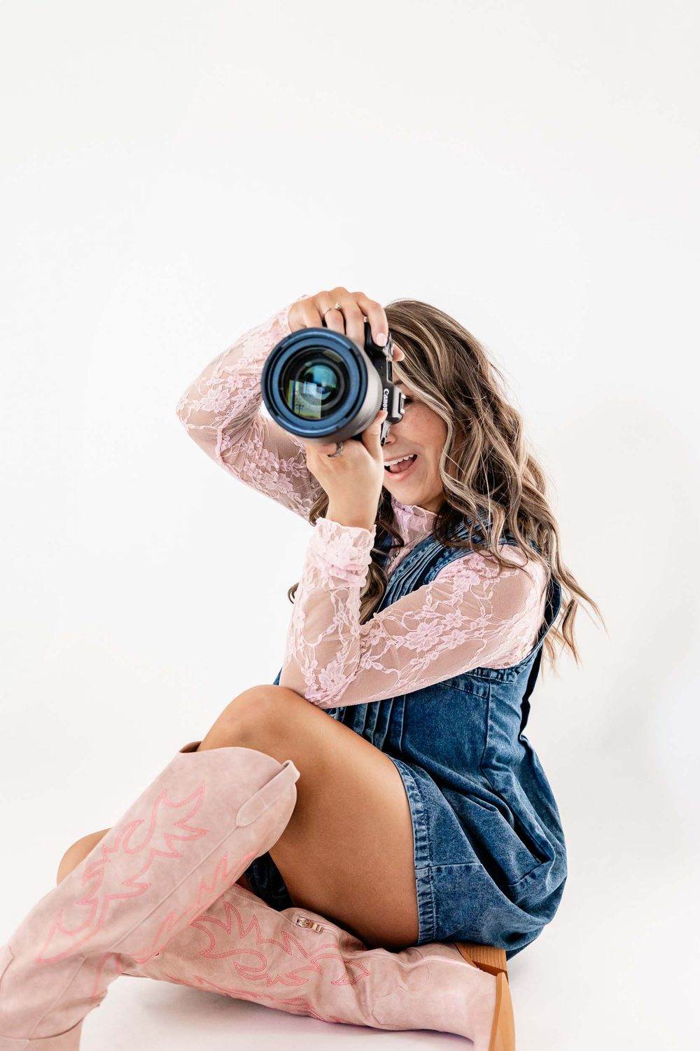 Wyoming Photographer
A photographer in a denim overalls dress, pink lacy top and matching boots holds up a professional camera lens.