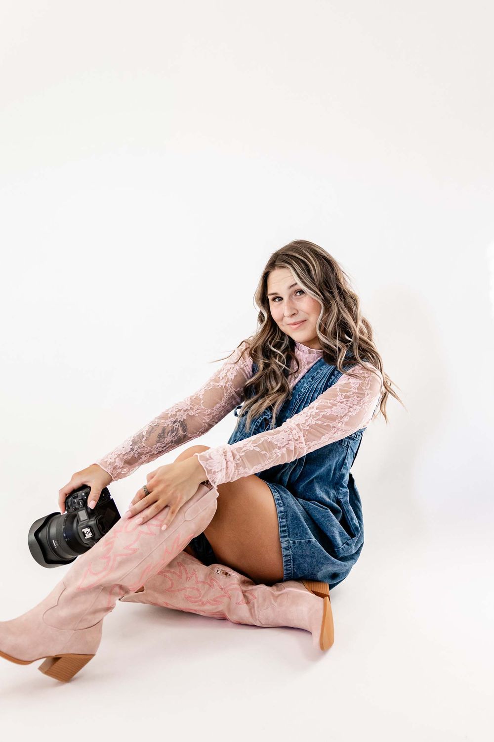Wyoming Photographer
Fashion model wearing pink lace sweater and denim overalls sits casually on white background with brown boots.