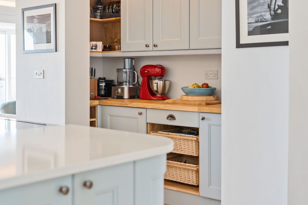 Light grey shaker kitchen with wooden worktops, wicker basket drawers, and a red KitchenAid mixer on the countertop.
