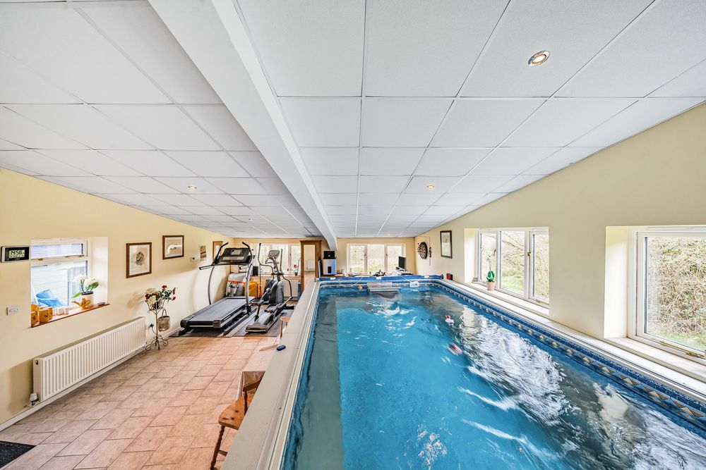 Indoor swimming pool and gym area with treadmill, tiled ceiling, and large windows in a private residential property.