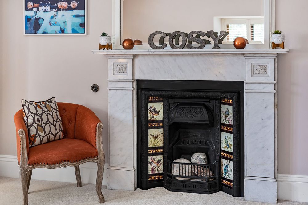 Elegant marble fireplace with decorative tiled insert, COSY letters on mantel, and vintage orange armchair in cozy living room.