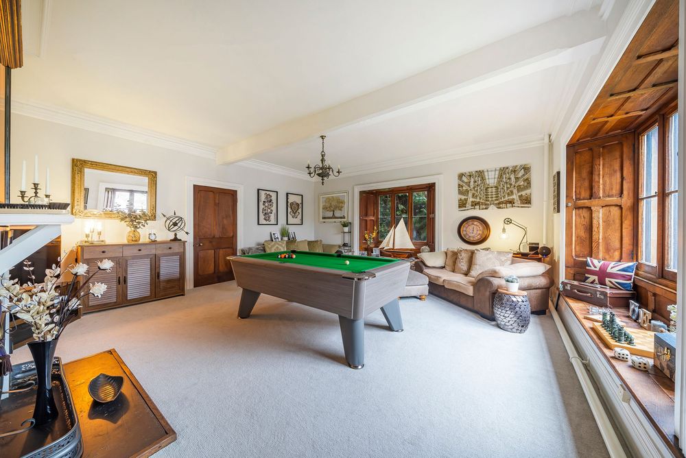 Elegant games room featuring a green baize pool table, plush sofas, ornate fireplace, and large windows with wooden shutters.