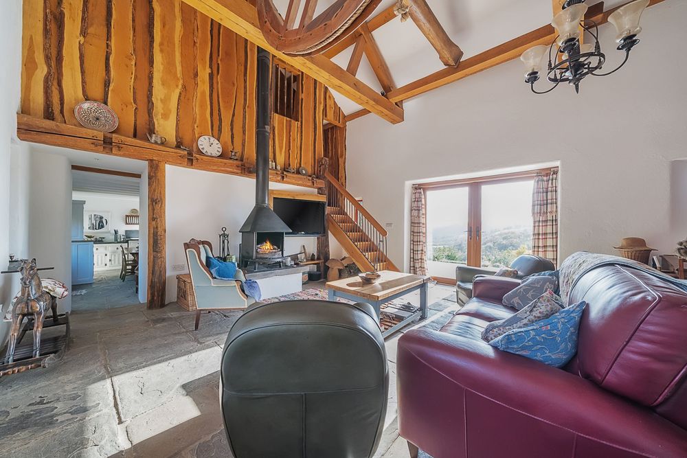 Rustic barn conversion living room with leather sofas, wood-burning stove, exposed beams, and mezzanine level with countryside views.