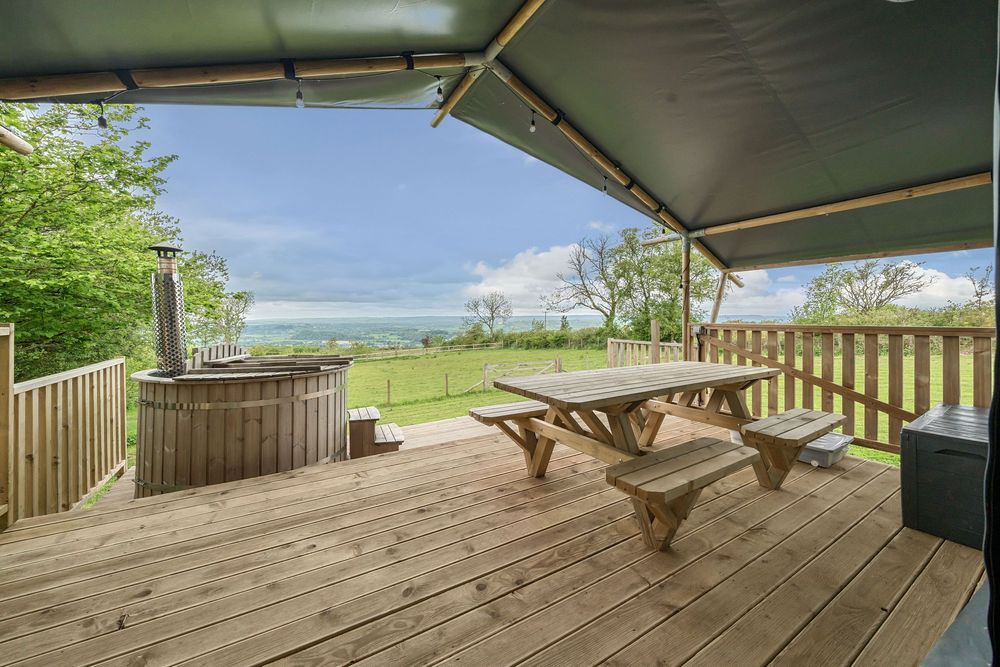 Covered deck with picnic table, wooden hot tub, and stunning countryside views under a canopy shelter.