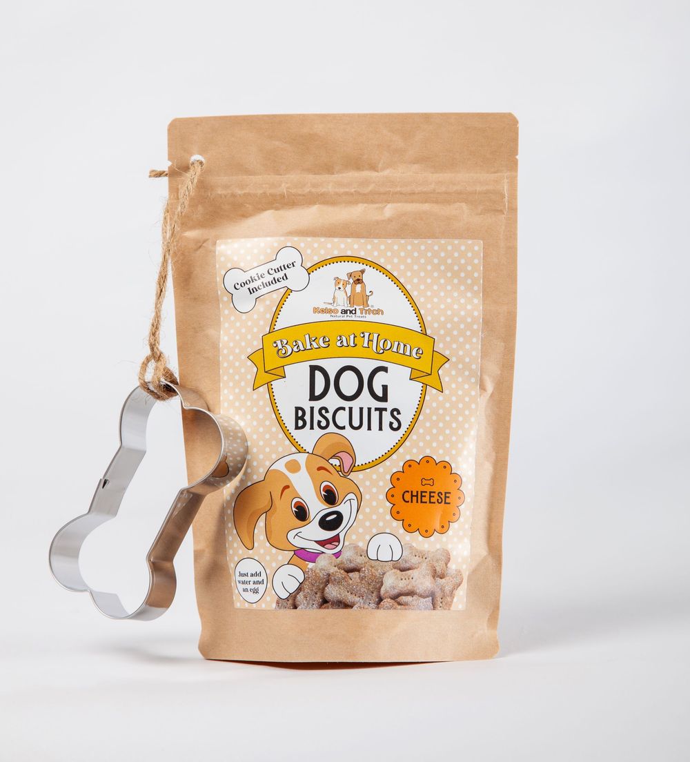 Bag of doggy biscuit mix with hanging bone shaped cookie cutter attached to bag, centred on a white background.