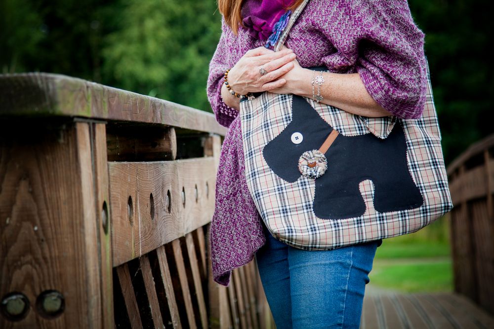 Handmade Shopper style bag with a black scotty dog symbol, worn by a woman with a pink jacket on. Set in an outdoor setting.