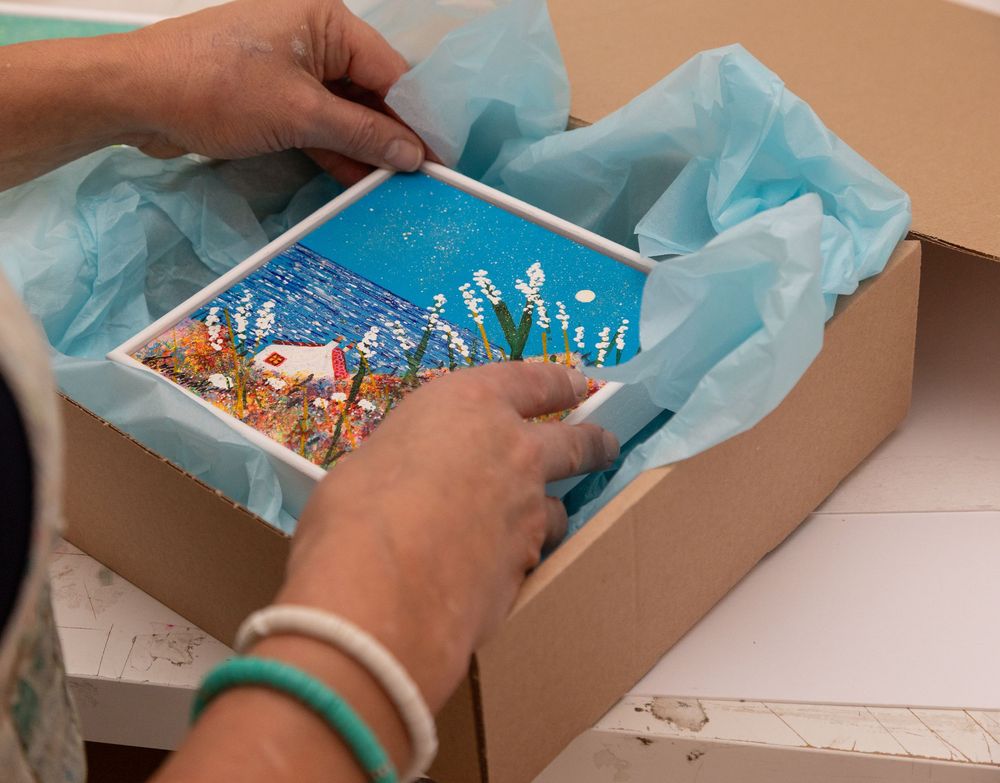 Hands placing a finished piece of artwork into a box for packaging and posting to client.