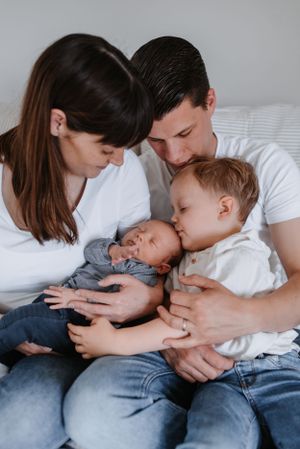 Parents cuddle with their newborn and toddler in tender family portrait.