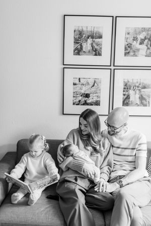 A black and white photo of a family sitting together on a couch beneath framed photographs on the wall.